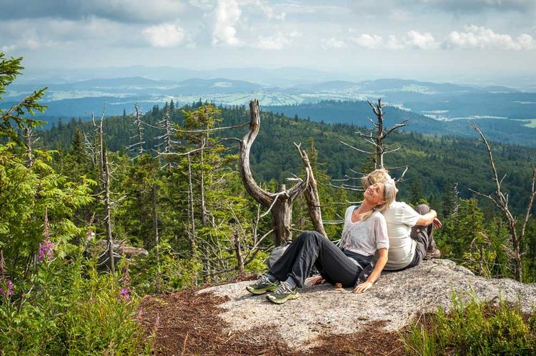 Zwei Wanderer sitzen auf einem Berggipfel mit einer Landschaft im Hintergrund