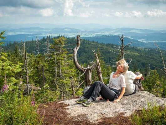 Zwei Wanderer sitzen auf einem Berggipfel mit Landschaft im Hintergrund